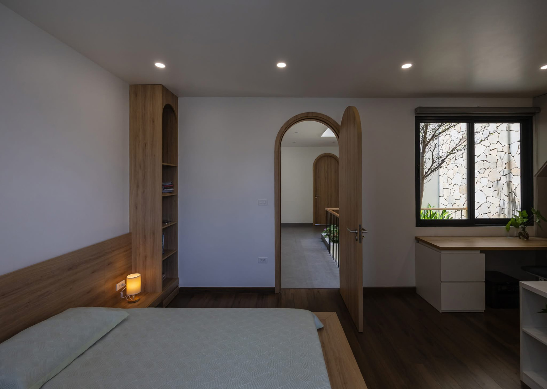 Bedroom with timber headboard, arched openings and desk by the window