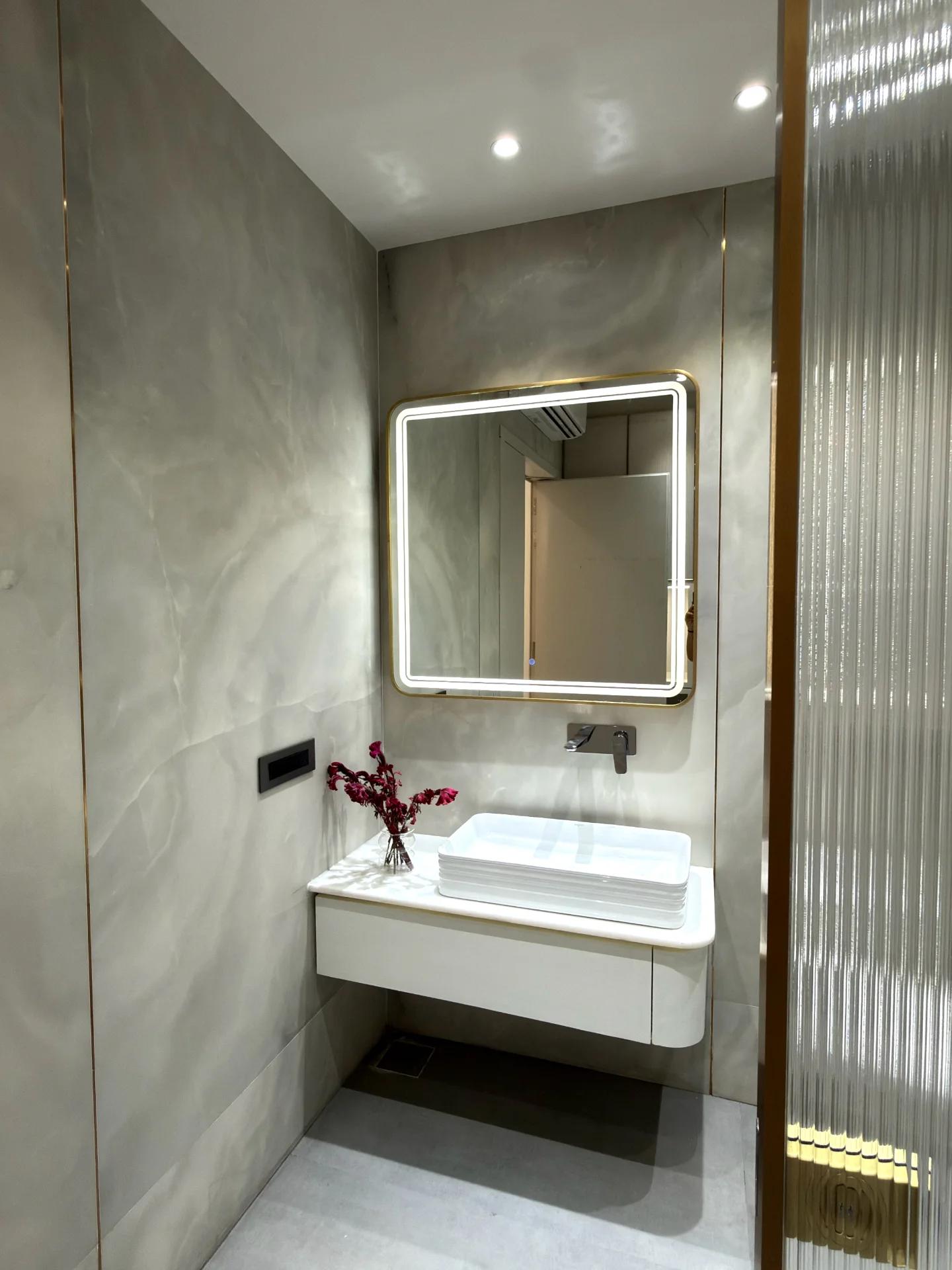 Powder room in onyx-veined stone with brass-framed backlit mirror