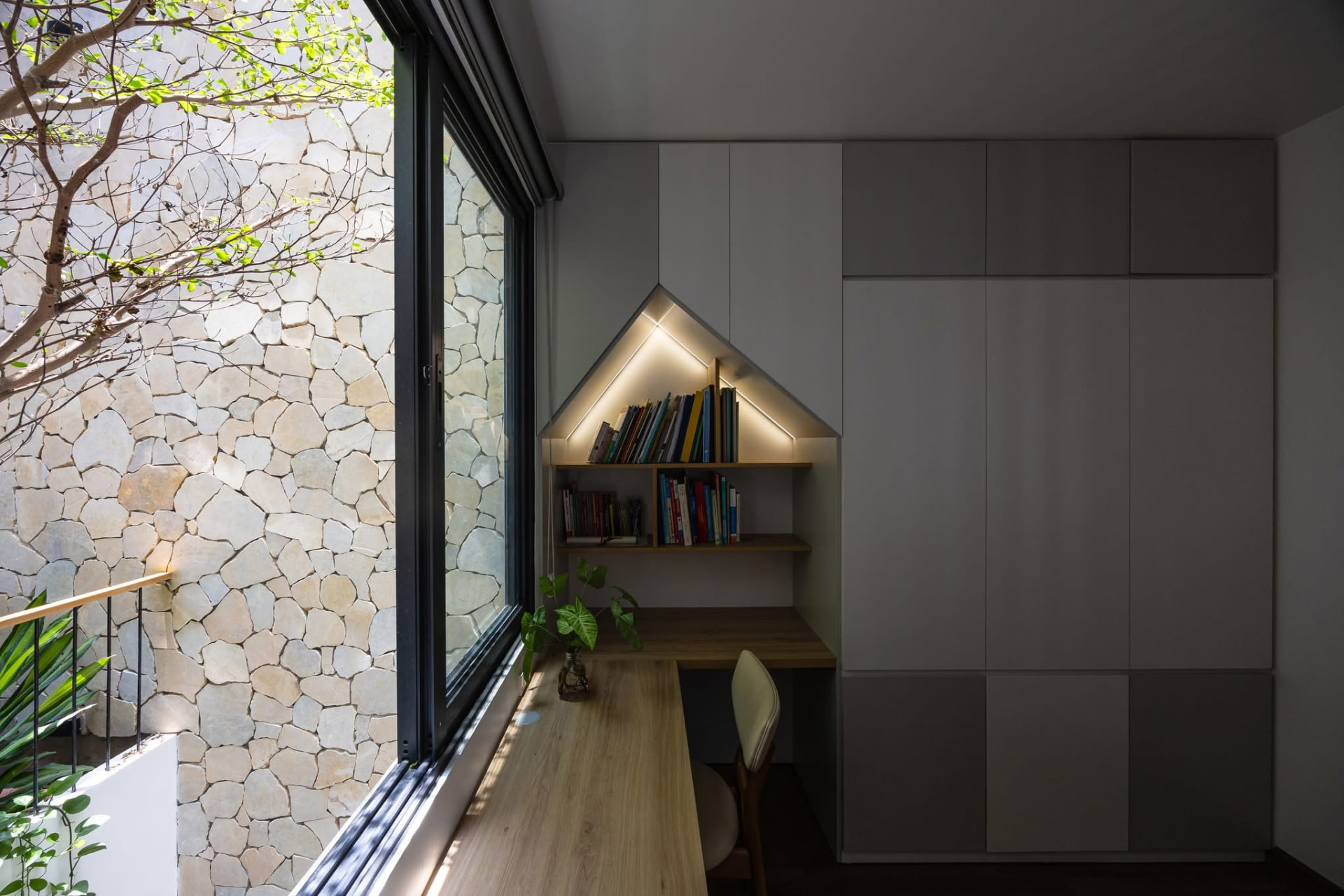 Study nook with gabled lit shelving beside a stone-clad courtyard