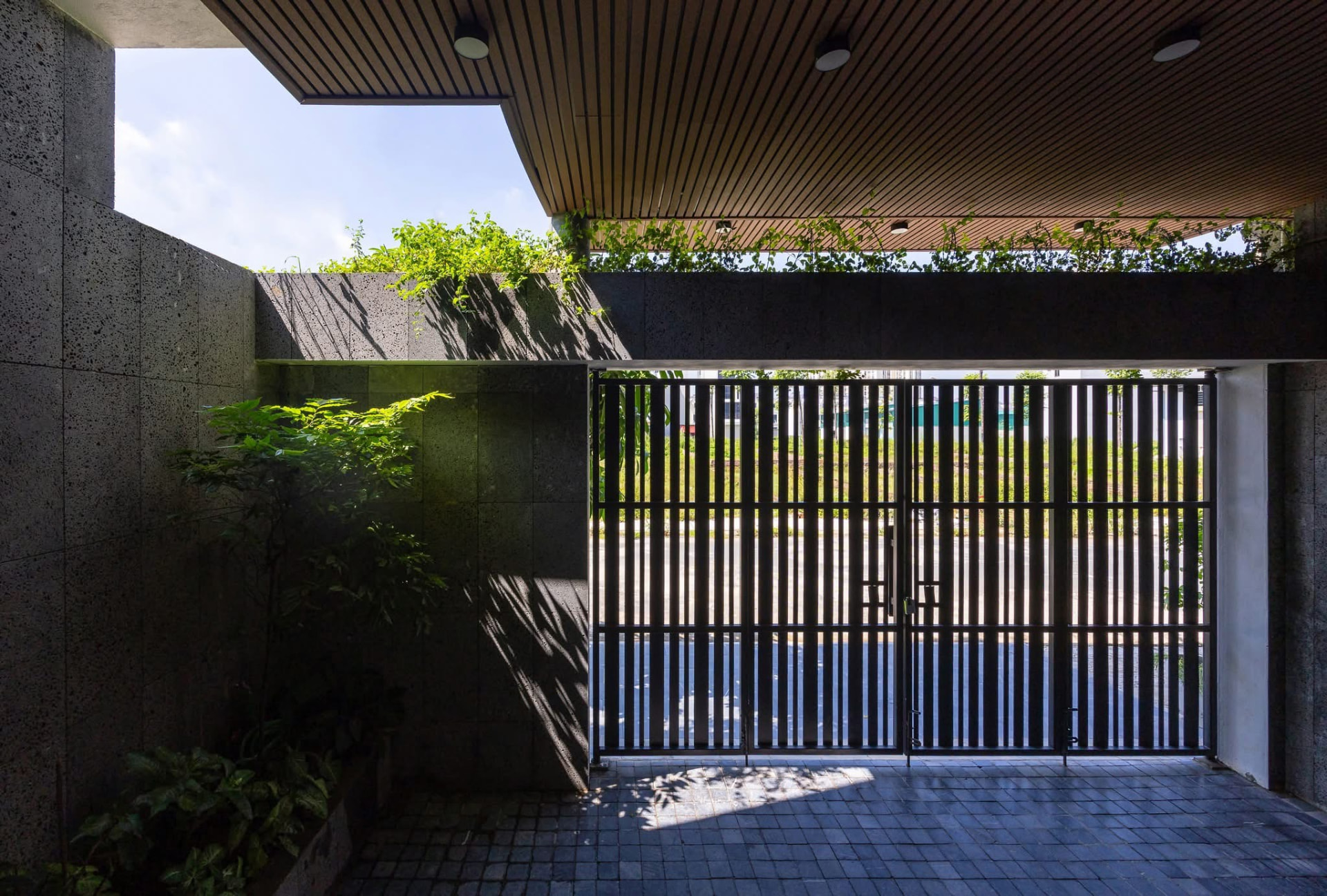 Entry forecourt seen through the slatted steel gate under a timber soffit