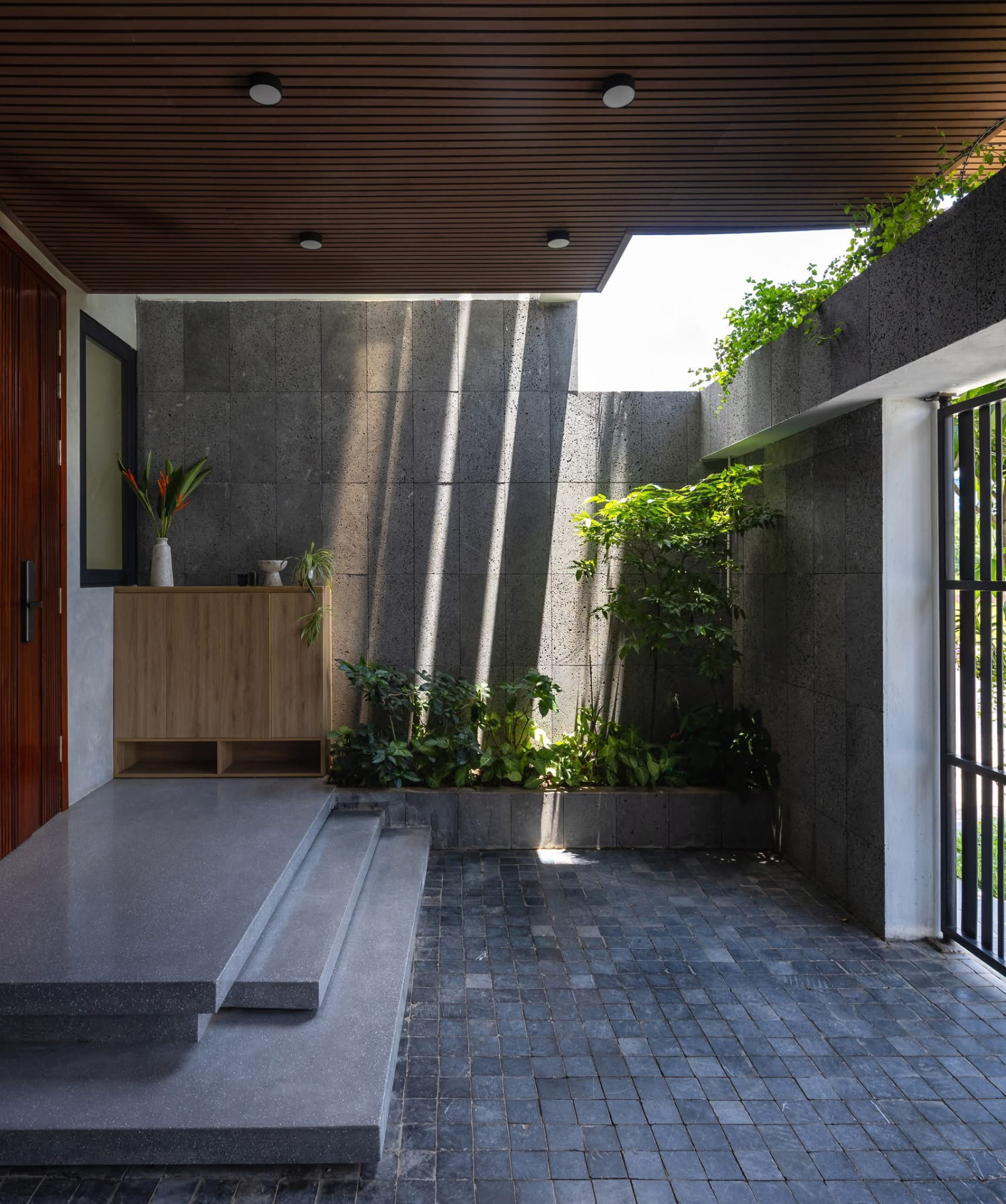 Entrance porch with teak door, lava stone wall and a planted bed